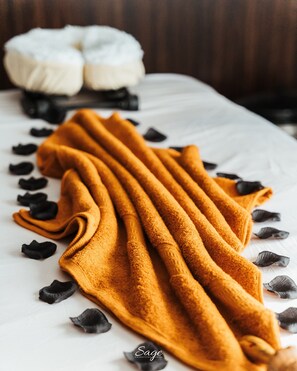 A bed with a white sheet, a mustard-colored towel, and black rose petals. - Kashco Apartment Wuse II (Abuja)