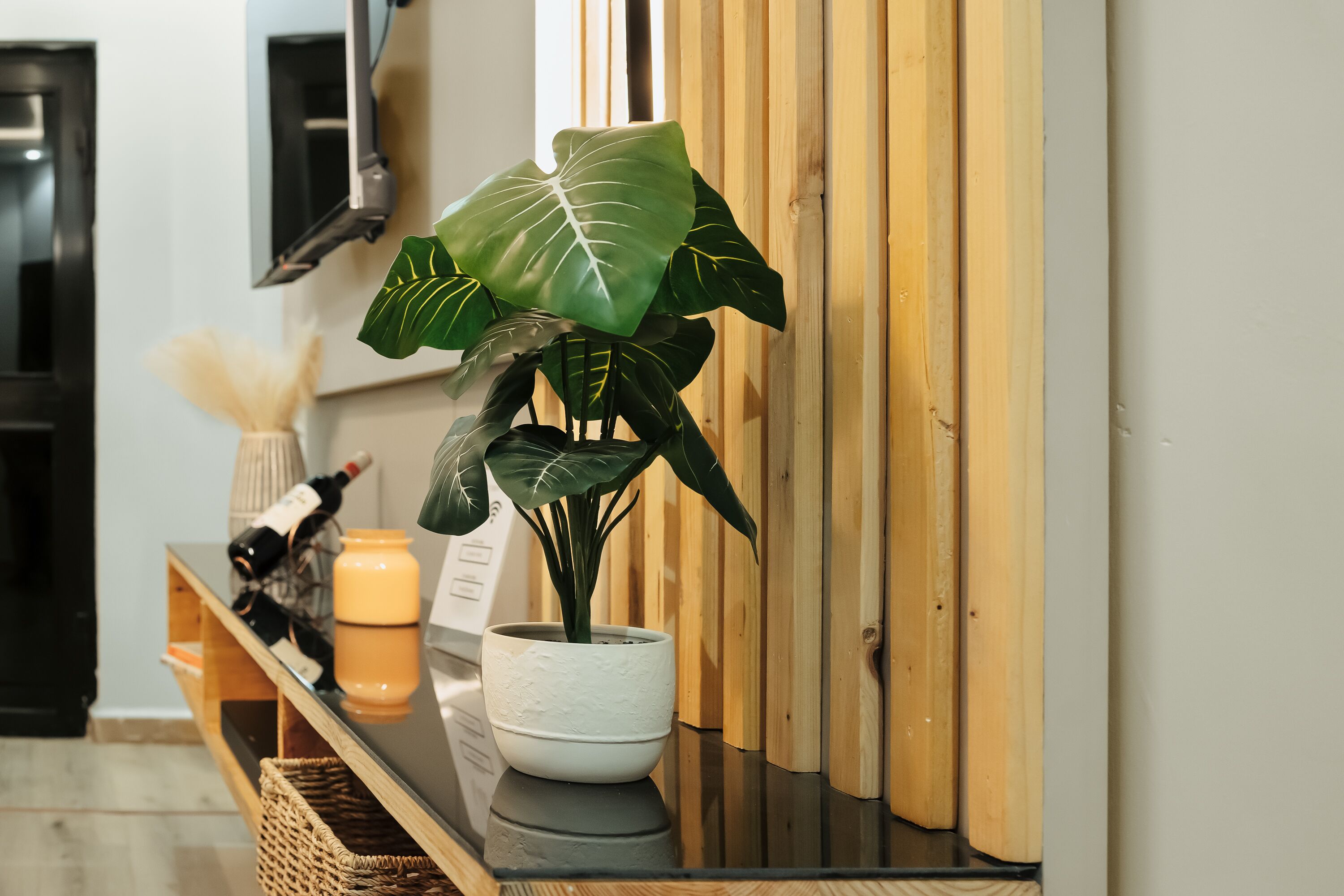 Une plante en pot, posée sur une table en bois, avec une bouteille et une bougie.