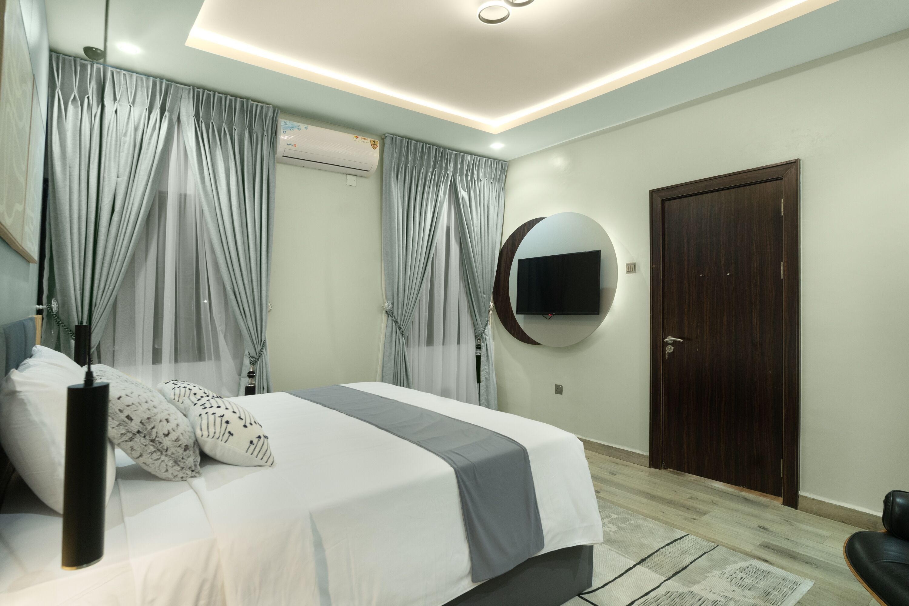 A modern bedroom with a bed, curtains, a mirror, and a door.