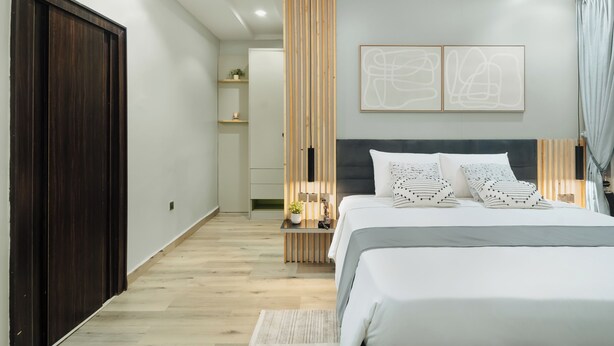 A modern bedroom with a large bed, bedside tables, a wooden partition, and abstract wall art. - Kashco Apartment Wuse II (Abuja)