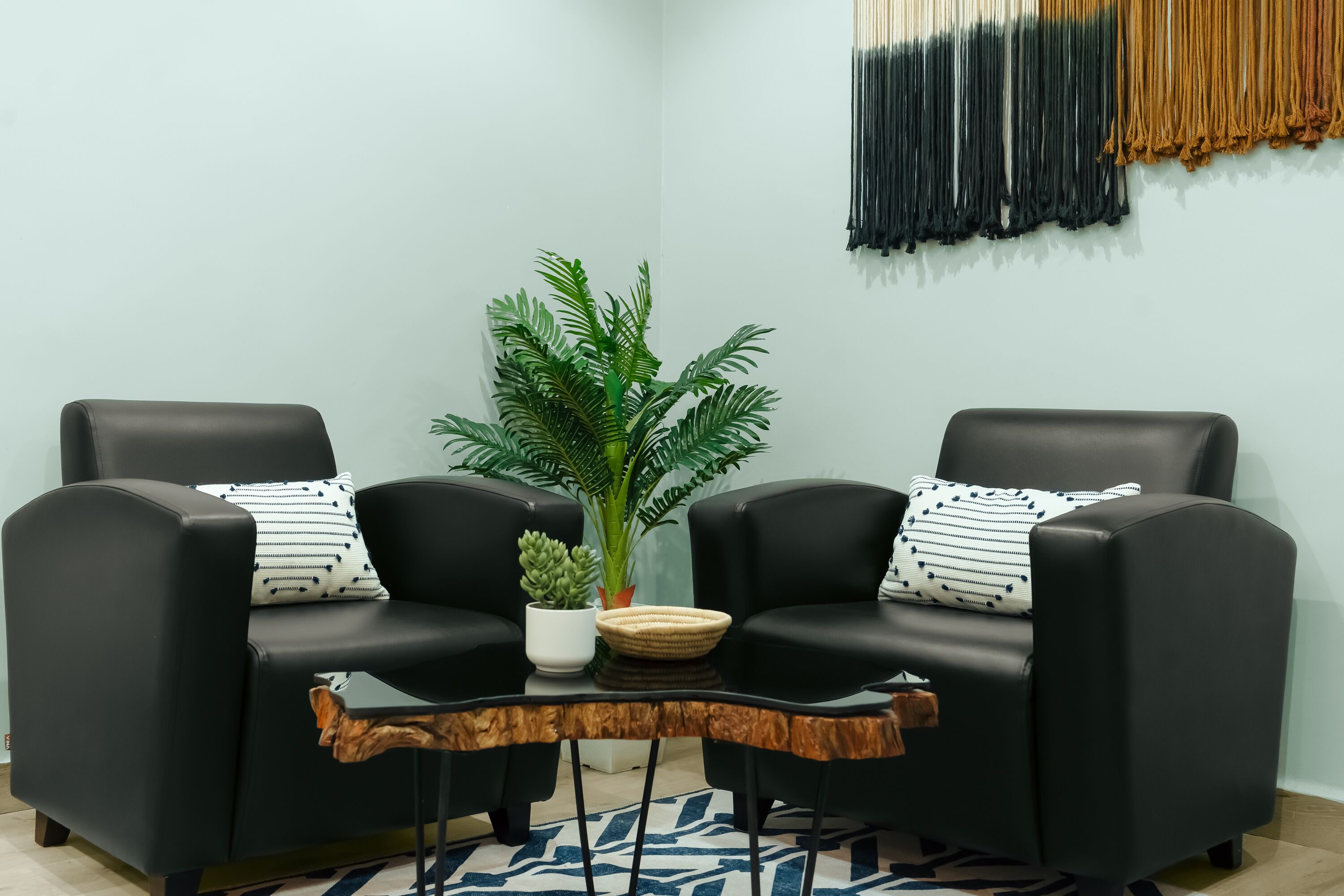 Un rincón con asientos: dos sillones de cuero negro, una mesita, una planta en maceta y una obra de arte en la pared.