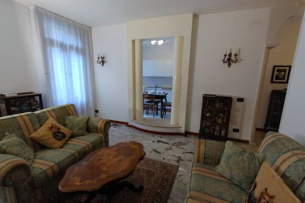 A living room with a sofa set, a coffee table, and a rug. There is a door leading to a dining area.