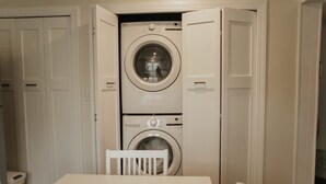 Une petite buanderie équipée d’un lave-linge et d’un sèche-linge superposés, d’une petite table et d’une chaise.