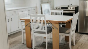 Une cuisine moderne avec des meubles blancs, une table à manger en bois et quatre chaises blanches aux pieds en métal.
