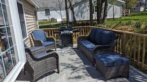 A covered patio with wicker furniture, a grill, and a view of neighboring houses. - Charming IU Cottage: Near Campus, Sleeps 8! (Bloomington)