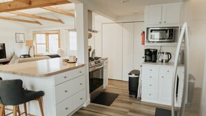 A modern kitchen with white cabinetry, a wooden countertop, and a built-in microwave. - Charming IU Cottage: Near Campus, Sleeps 8! (Bloomington)