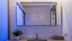 A modern bathroom with a large mirror, a sink, and a potted plant. - Agora Apartments   Sea View Apartment (Sorrento)