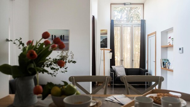 A dining area with a table set for two, a vase of flowers, and a view of a balcony with a sofa. - Agora Apartments   Sea View Apartment (Sorrento)