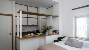 A compact bedroom with a bed, a bedside table with a plant, and a built-in desk with a coffee machine. - Agora Apartments   Sea View Apartment (Sorrento)
