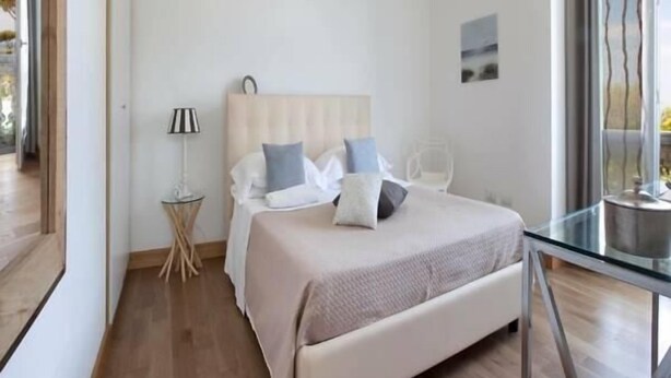 A modern bedroom with a bed, bedside table, lamp, and a view of the outdoors.