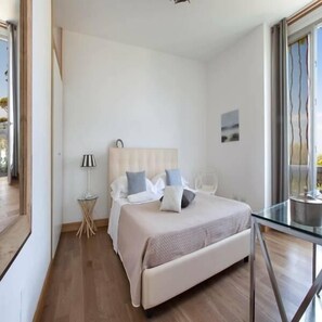 A modern bedroom with a bed, bedside table, lamp, and a view of the outdoors.