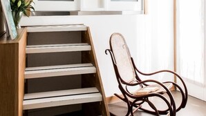 A staircase with a wooden handrail and white steps, a wicker rocking chair, and a framed picture on a shelf.