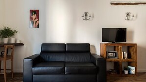 A black leather sofa in a living room with a wooden coffee table, a TV on a wooden stand, and a potted plant. - Agora Apartments Armida street view (SORRENTO)