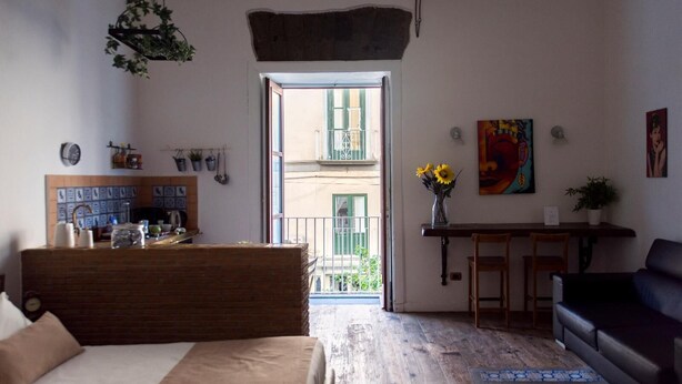 A cozy room with a bed, a desk, a chair, and a couch. There is a window with a view of a balcony and a building. - Agora Apartments Armida street view (SORRENTO)