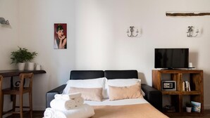 A hotel room with a bed, a desk with a chair, a television, and a bookshelf. - Agora Apartments Armida street view (SORRENTO)