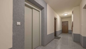 A hallway with a tiled floor, a door with a light switch, and a wooden door at the end. - Modern Studio with Balcony | Close to Nature (Katowice)