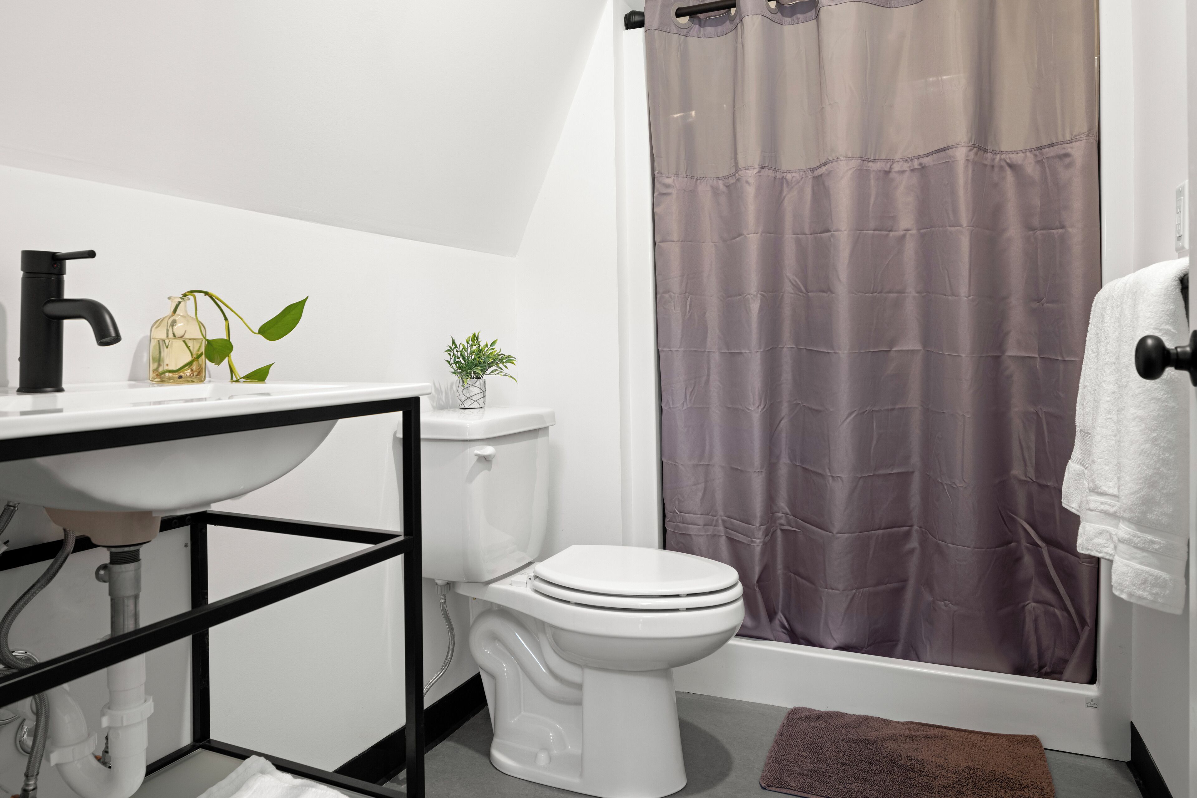 A bathroom with a white sink, black faucet, toilet, and a shower curtain.