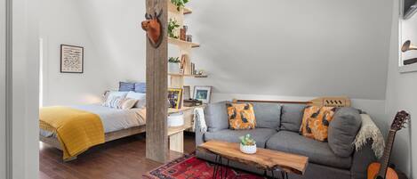 Una sala de estar moderna con una cama, un sofá gris, una mesa de centro de madera y una guitarra.