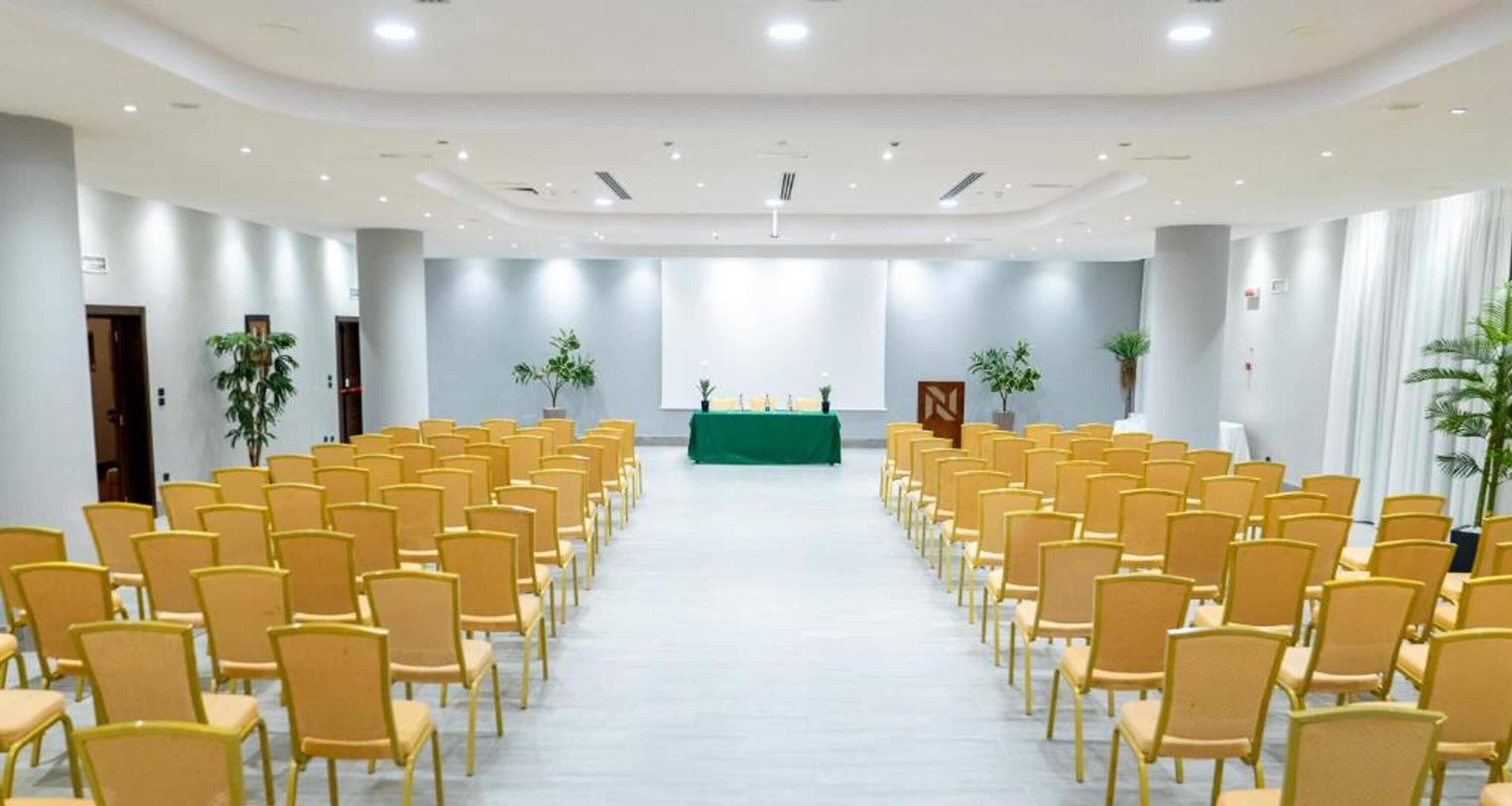 A conference room with rows of chairs, a podium, and potted plants.