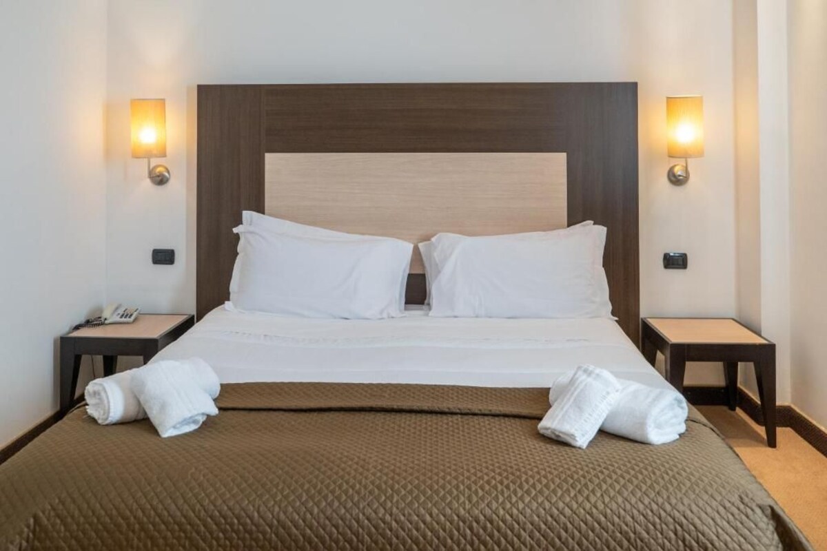 A hotel room with a large bed, two bedside tables, and wall-mounted lamps.