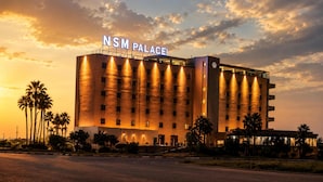Een hotel met een modern design, genaamd 'NSM Palace', met een opvallend bord, meerdere verdiepingen en een goed verlichte gevel.
