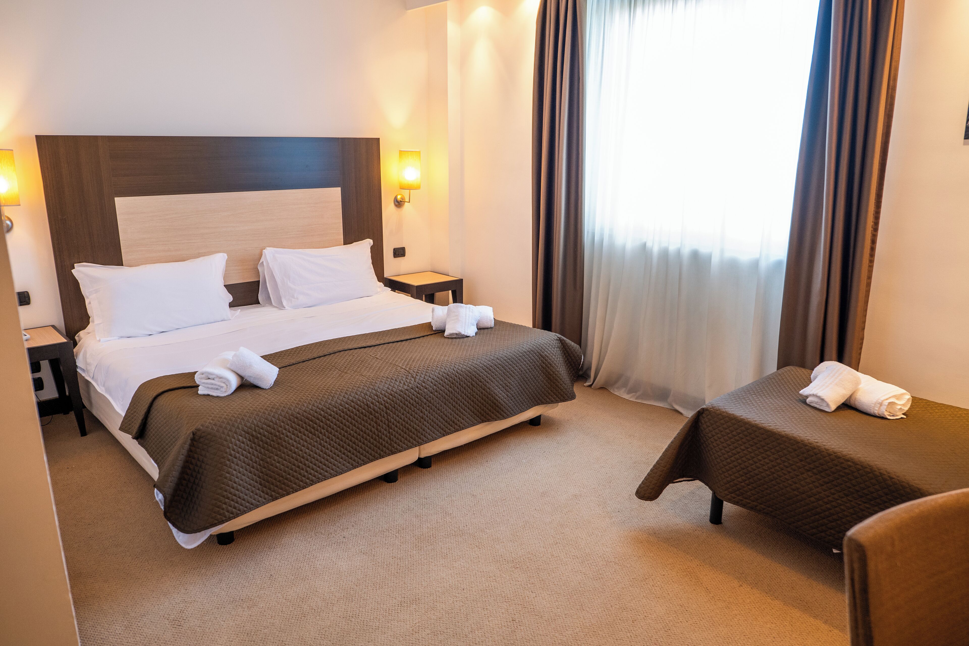 Une chambre d’hôtel avec un grand lit, deux tables de chevet, un petit canapé et une fenêtre avec des rideaux.