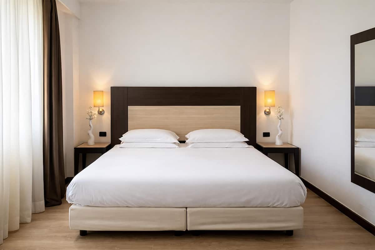 Un lit double avec une tête de lit en bois, deux tables de chevet avec des lampes et un grand miroir au mur.