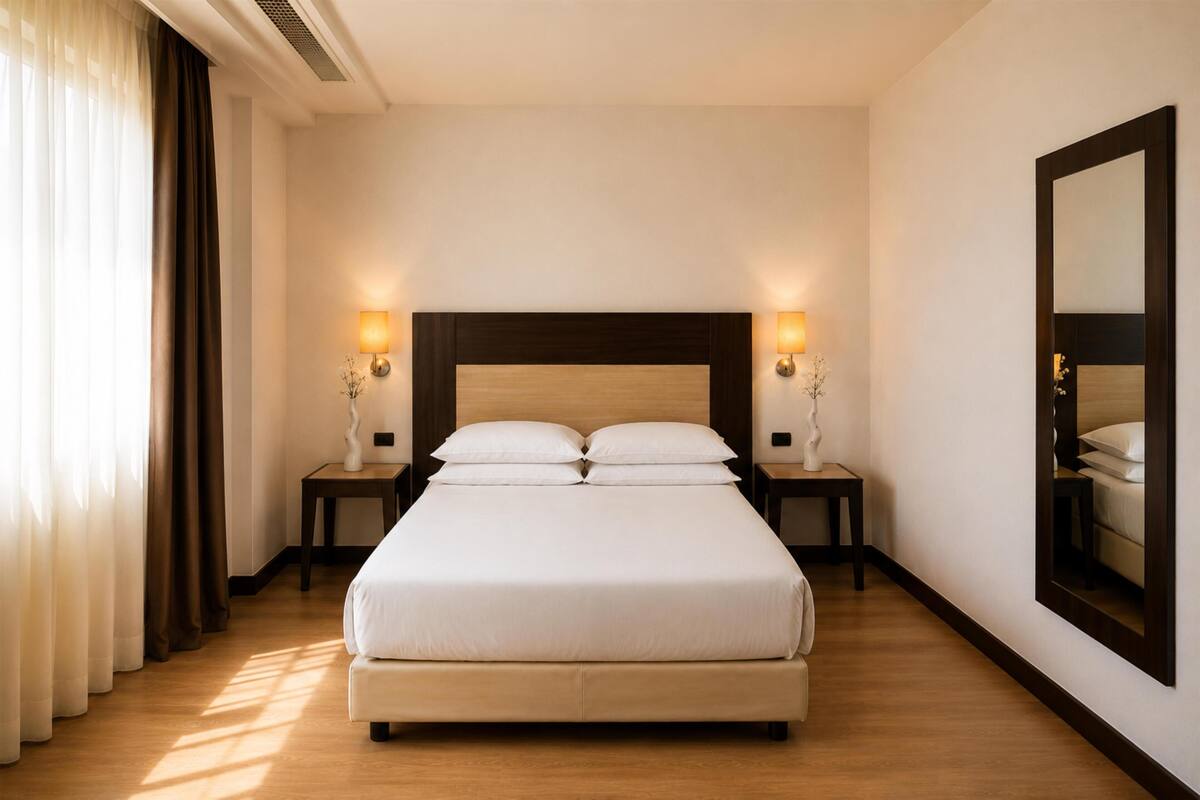 Une chambre d’hôtel avec un grand lit, deux tables de chevet, une commode, un miroir et une fenêtre avec des rideaux.