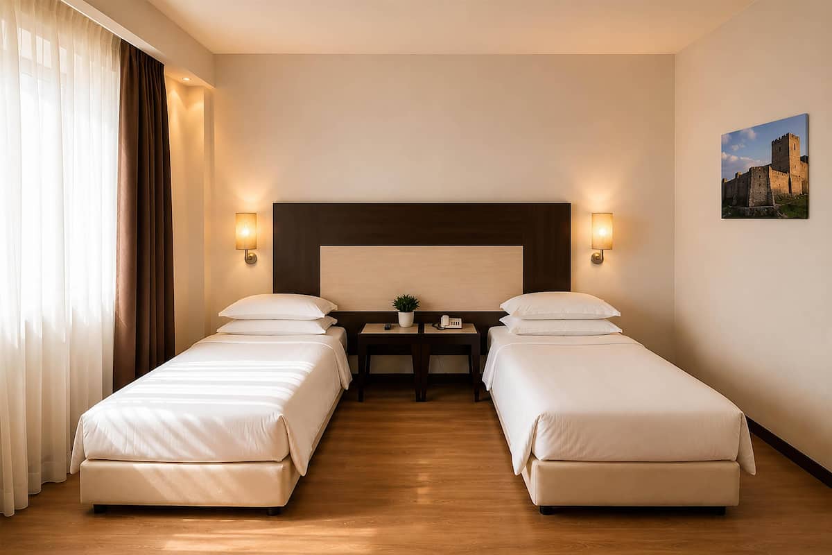 Une chambre d’hôtel avec deux lits simples, un plancher en bois, une table de chevet avec une lampe et un tableau au mur.
