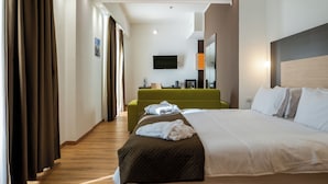 Een hotelkamer met een groot bed, een groene bank, een flatscreen televisie aan de muur en een spiegel boven de bank.