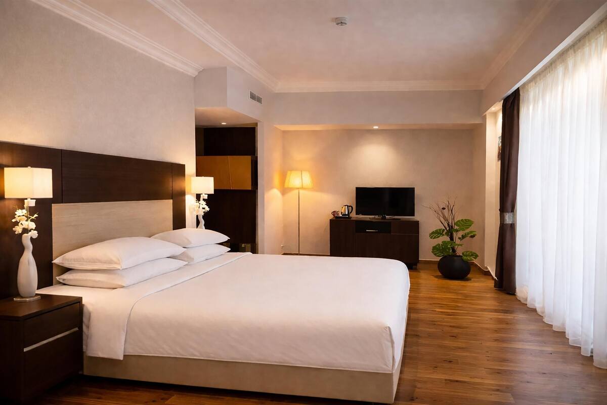 Une chambre d’hôtel avec un grand lit, des lampes de chevet, une télévision, une plante en pot et un plancher en bois.