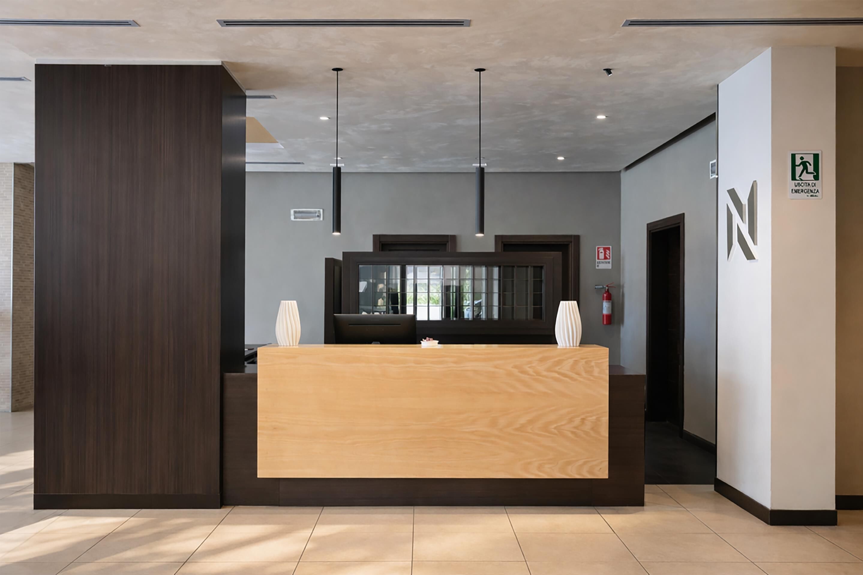 A reception desk with a wooden finish, pendant lighting, and a glass partition.
