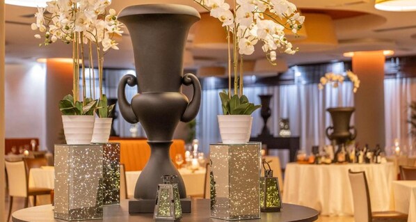 Una mesa de comedor con un jarrón grande, plantas en macetas y recipientes de vidrio decorativos.