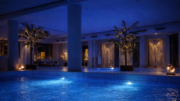 Een binnenzwembad met verlichting, palmbomen en een modern interieur.