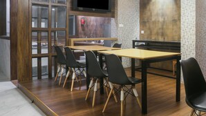 Une salle de conférence avec une table en bois et des chaises noires, un extincteur et un téléviseur fixé au mur.