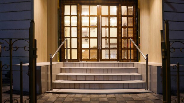 Un escalier extérieur mène à une porte en bois dotée de panneaux de verre, et est bordé de rampes de garde-corps en métal.