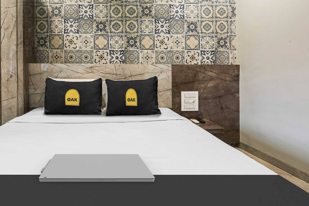 Een bed met een laptop, twee kussens met de tekst 'OAK' en een betegelde muur met een patroon.