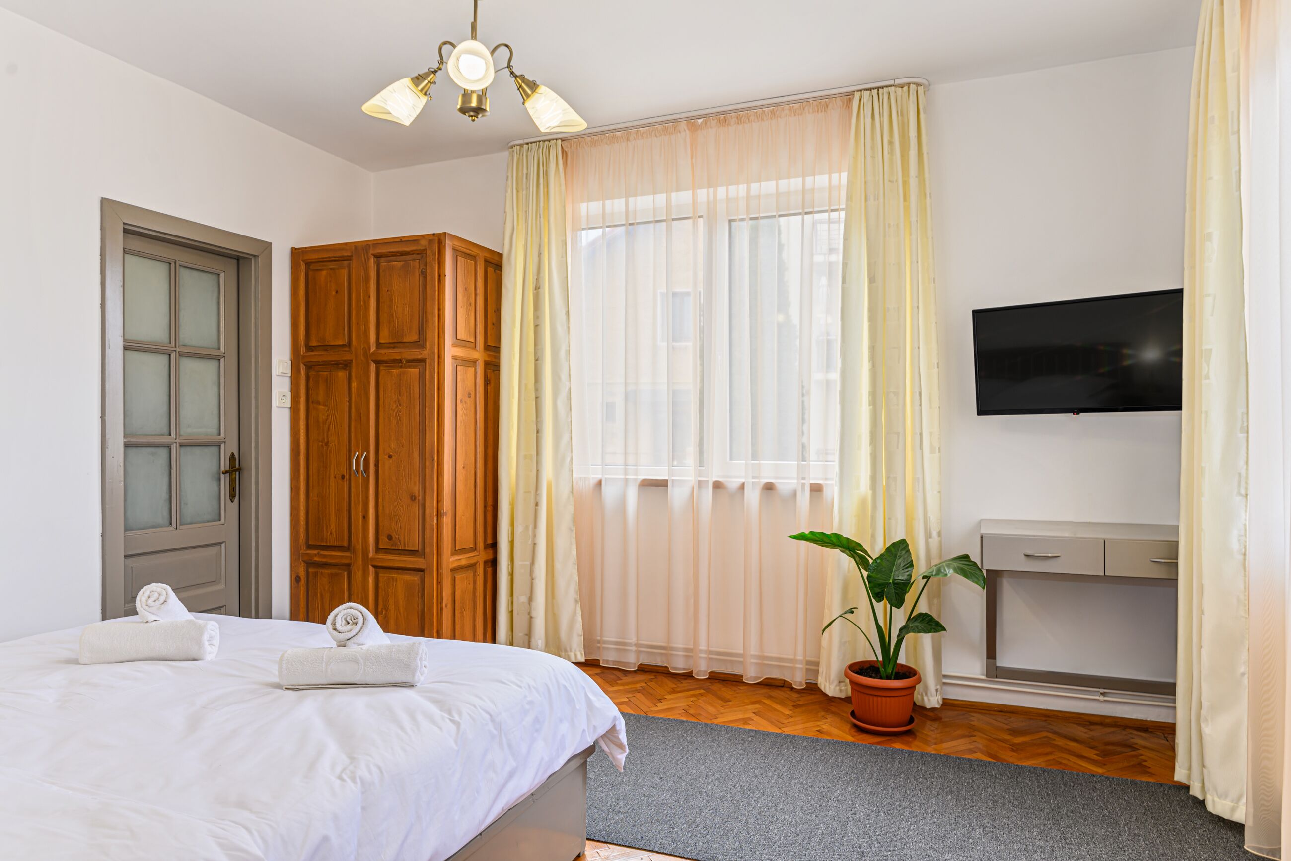 Ett hotellrum med en säng, en garderob i trä, en tv på väggen och en krukväxt.