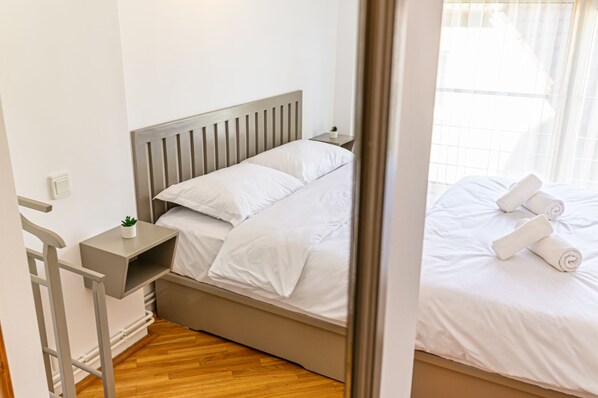 Quarto com cama, mesa de cabeceira com planta e janela com cortinas.