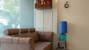 A brown sofa in a room with a tiled floor, a water dispenser, and a security camera on the wall. - AR Residency (Mumbai)