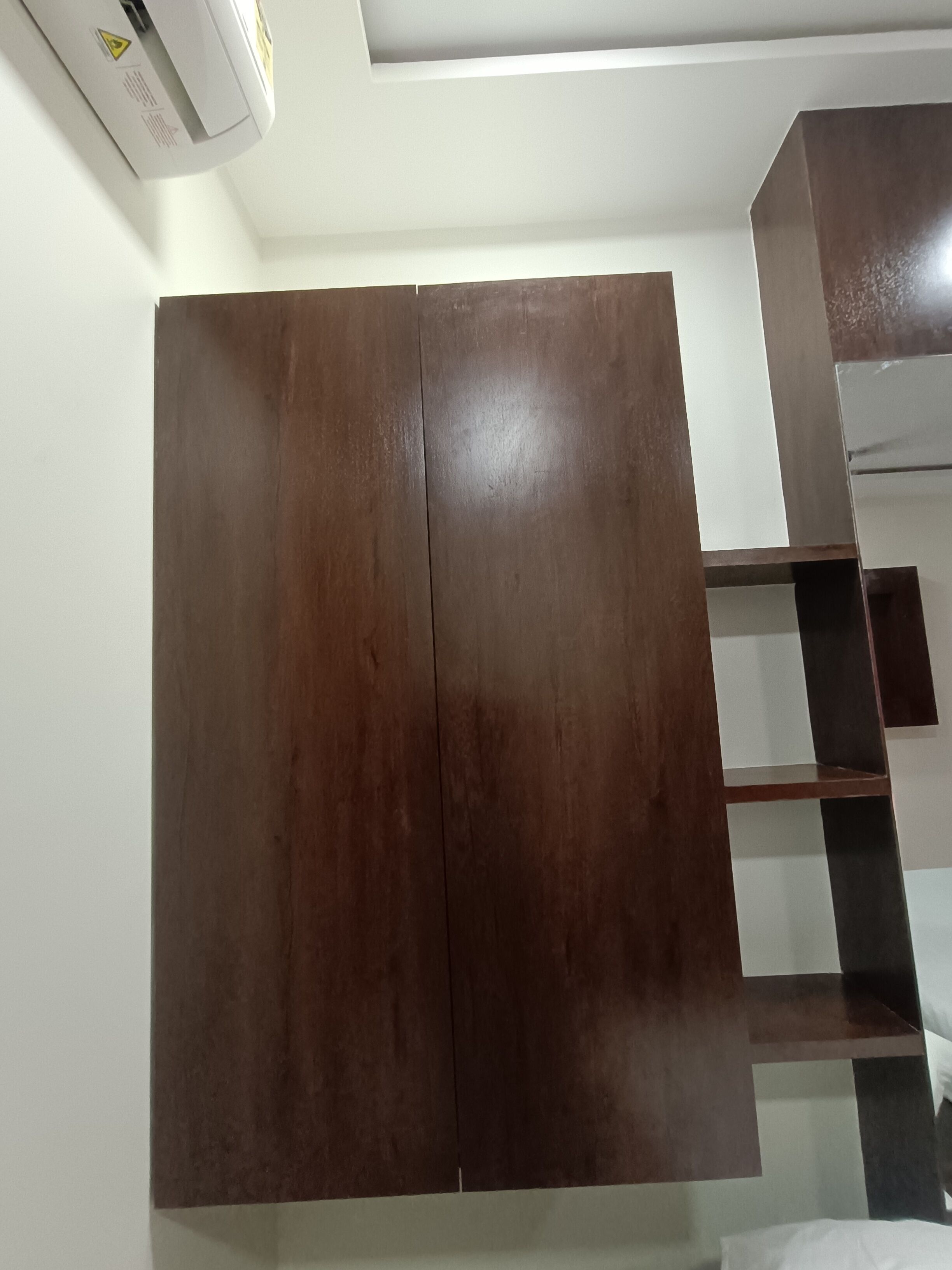 A room with a large wooden wardrobe, a white ceiling, and a partial view of a staircase.