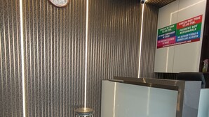 A reception area with a modern design, featuring a clock, a ceiling fan, and a sign with check-in times and rules. - AR Residency (Mumbai)