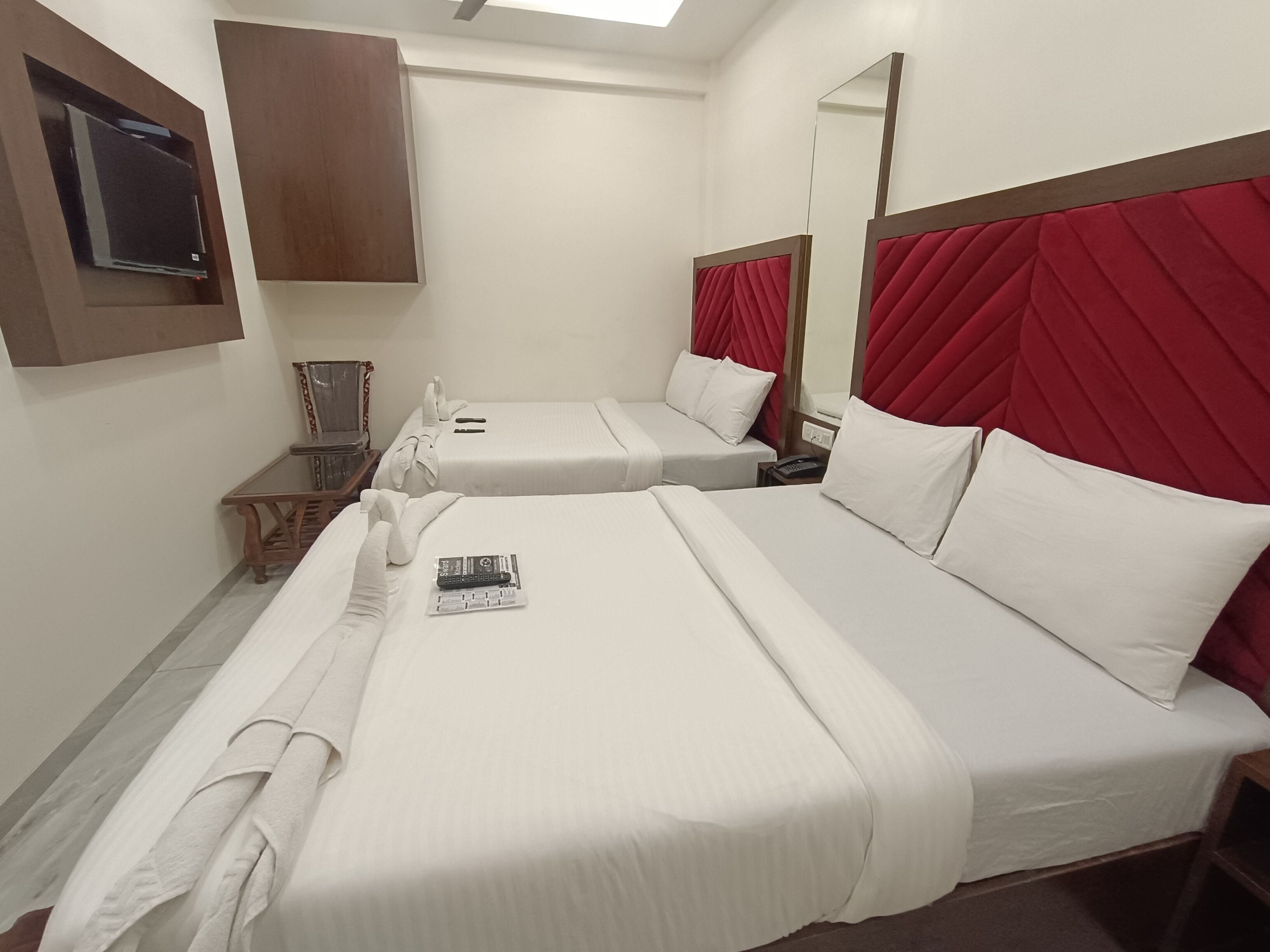 A hotel room with two beds, a wooden chair, a small table, a mirror, and a TV mounted on the wall.