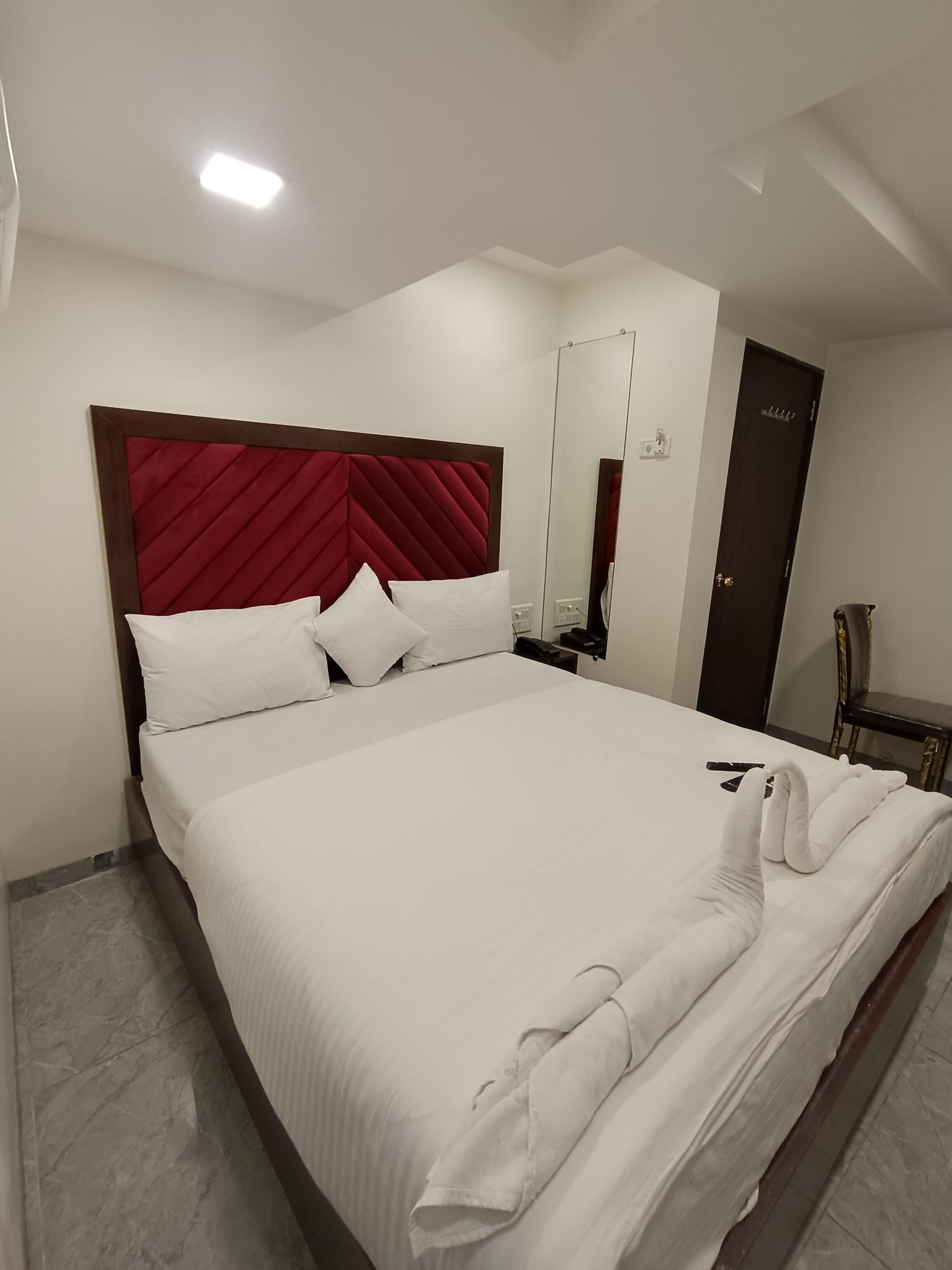 A neatly made bed with white linens and a red headboard in a hotel room.