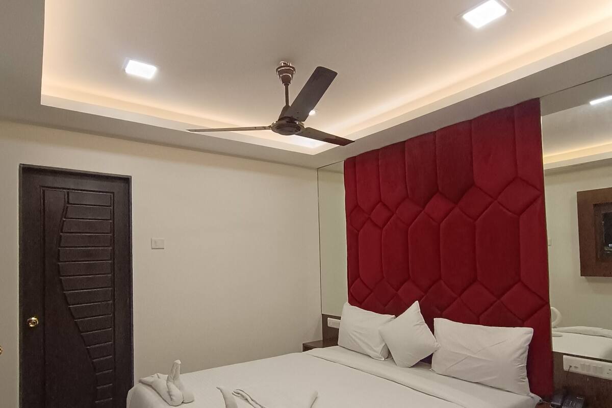 A neatly made bed with white linens and towels, a red headboard, a ceiling fan, and a modern light fixture.