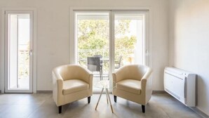 Un salon moderne avec deux fauteuils beiges, une table basse en verre et un radiateur blanc.