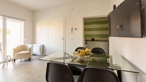 Un espace repas moderne avec une table en verre, des chaises noires et un saladier rempli de fruits.