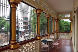 A covered balcony with metal railings, a white table, and two chairs. - Shiv Sadan Palace 1940 (Varanasi)