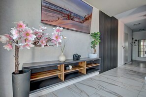 A modern living room with a large flat-screen TV mounted on the wall, a wooden console table with decorative items, and a potted plant.