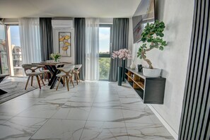 A modern dining area with a marble floor, a round table, and chairs. There is a large window with curtains, a wall-mounted air conditioner, and a potted plant on a shelf. - HelApart - Kaszubska Bryza II (Hel)